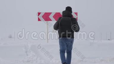 徒步旅行者带着背包，在道路上的冬天选择在两个不同的道路方向之间的道路岔路口。 概念